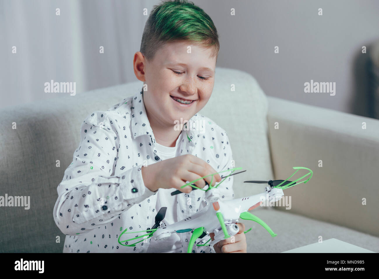 Smiling boy adjusting drone while sitting on sofa at home Stock Photo