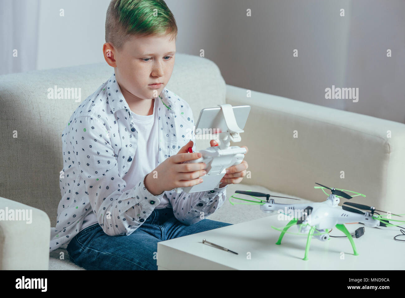 Boy using remote control sitting on sofa by drone on coffee table at home Stock Photo