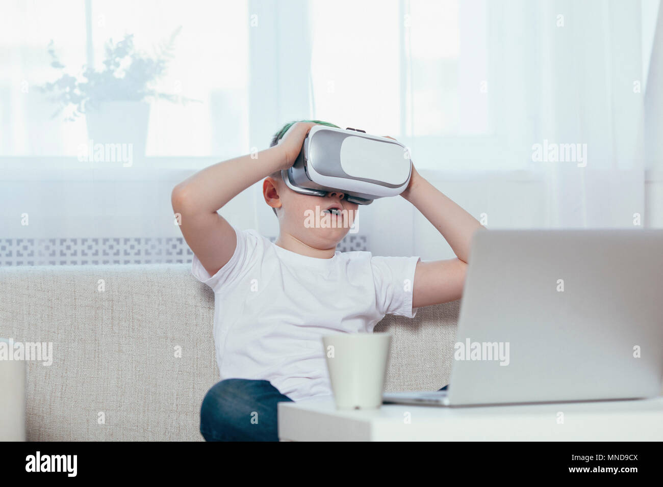 Boy wearing virtual reality headset while sitting on sofa at home Stock Photo