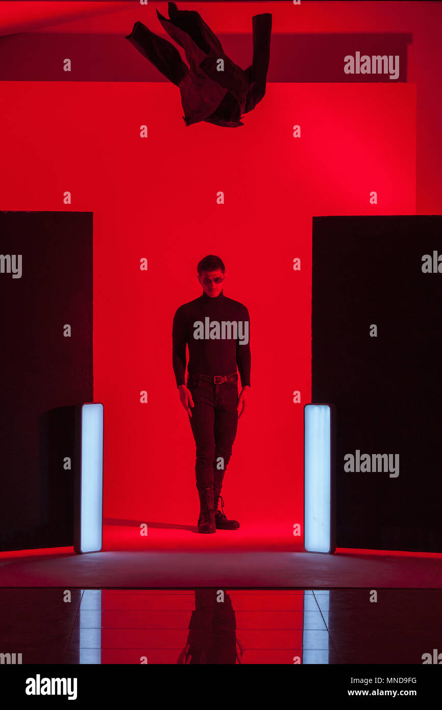 Full length of young man standing below falling jacket amidst illuminated lights in red studio Stock Photo