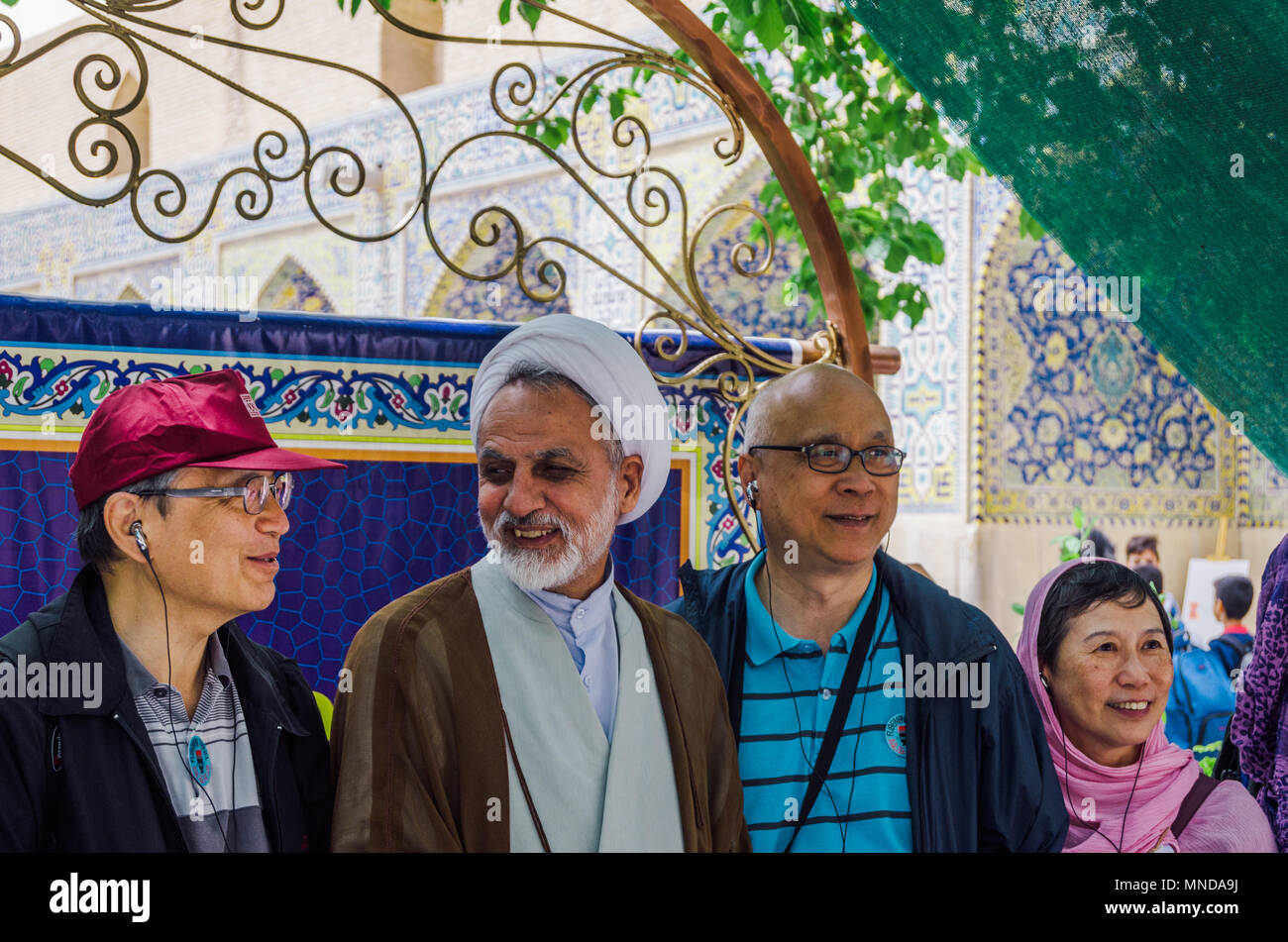 Isfahan, Iran - April 23, 2018: An older Iranian Mullah wearing a keffiyeh poses with tourists in the courtyard of the Jame Mosque Stock Photo