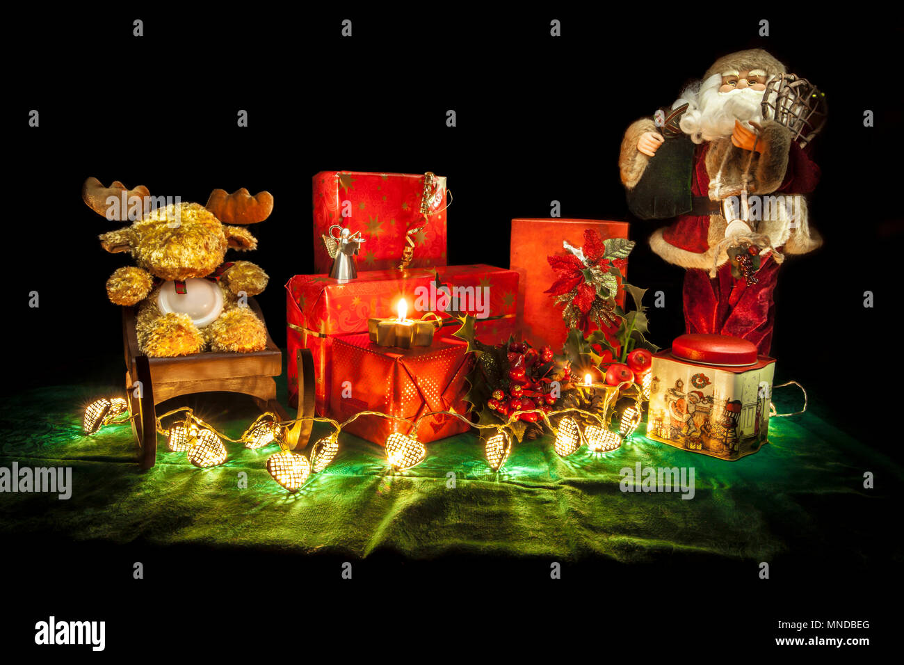 Christmas still life composition with Santa Claus puppet, a reindeer puppet on a sledge, heart-shaped christmas tree lights, two candles, some red gif Stock Photo