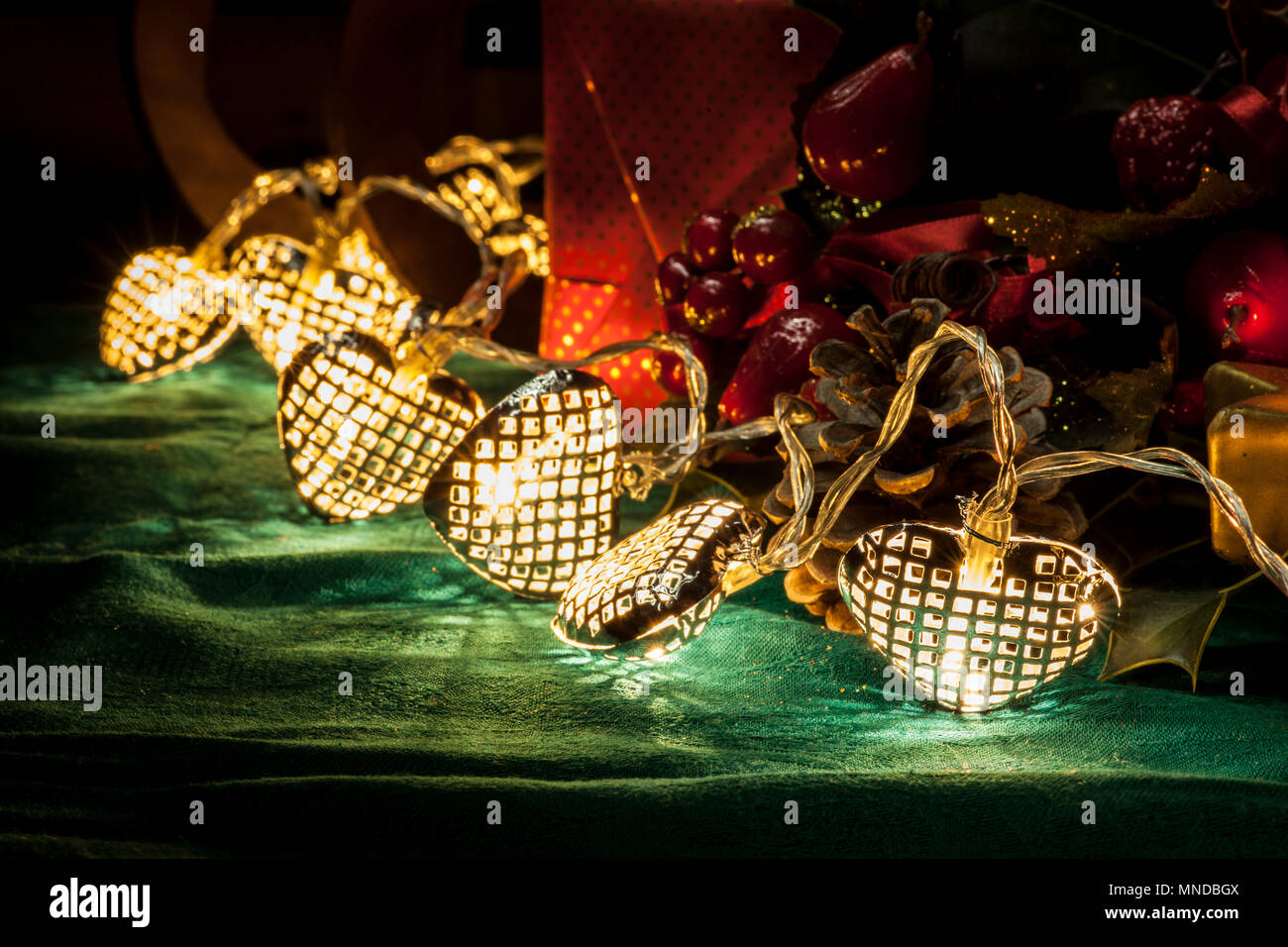 Christmas still life composition with heart-shaped christmas tree lights, a red gift box, some red fruits and a pine cone. The christmas tree lights m Stock Photo