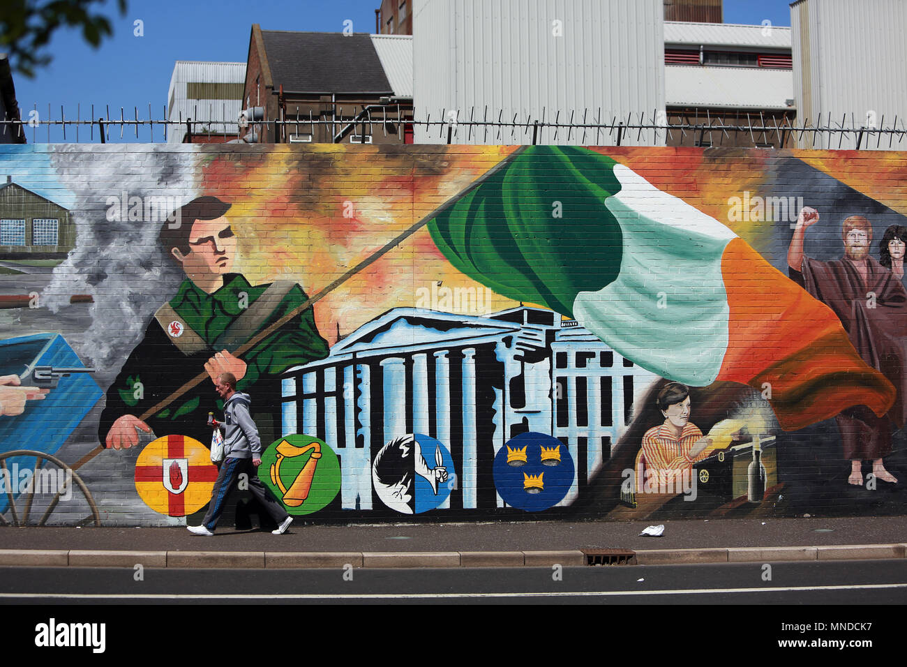 A man walks past the international peace wall on the Falls Road, west Belfast, May 2018. The Falls Road (from Irish túath na bhFál, meaning 'territory of the enclosures) is the main road through west Belfast, Northern Ireland, running from Divis Street in Belfast city centre to Andersonstown in the suburbs. Its name is synonymous with the republican community in the city, whilst the neighbouring Shankill Road is predominantly loyalist, separated from the Falls Road by peace lines. The road is usually referred to as the Falls Road, rather than as Falls Road. It is known as the Faas Raa in Ulste Stock Photo