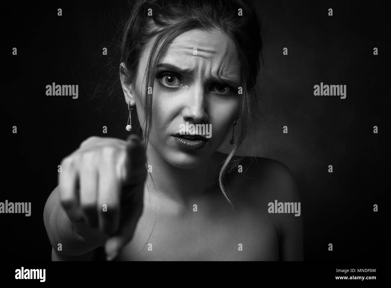 angry young woman on black background point on camera, monochrome Stock Photo