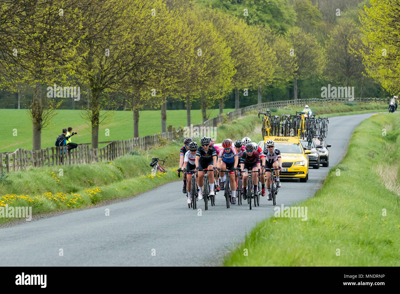 Team support cars & cyclists in pack, competing in Tour de Yorkshire 2018, racing on scenic countryside lane - Ilkley, North Yorkshire, England, UK. Stock Photo