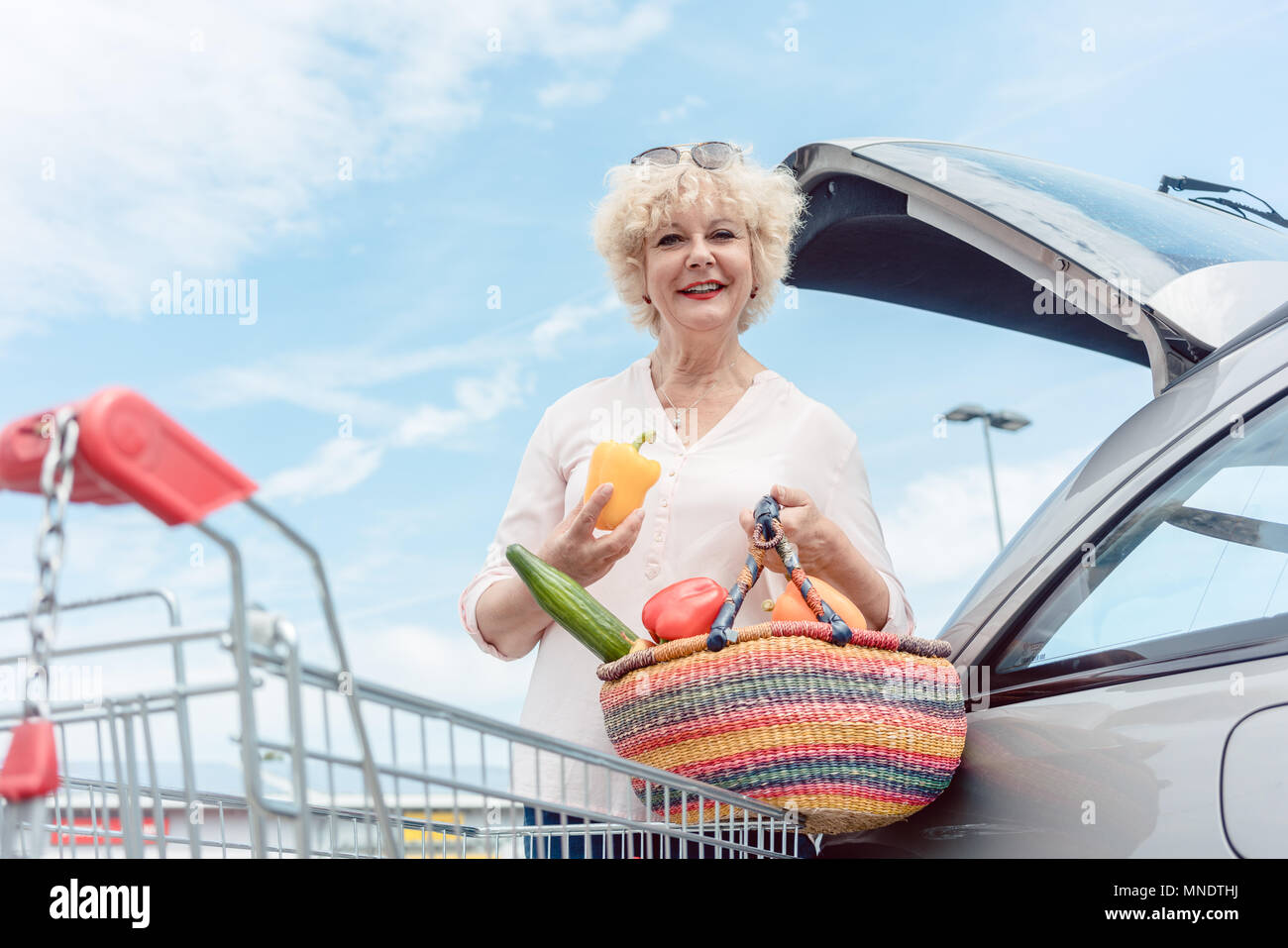 Cheerful senior woman holding a basket full of fresh vegetables  Stock Photo