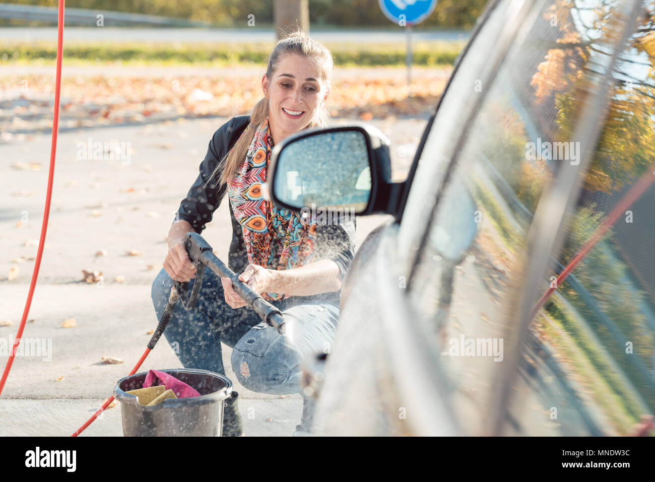 Woman using high pressure nozzle to clean her car Stock Photo