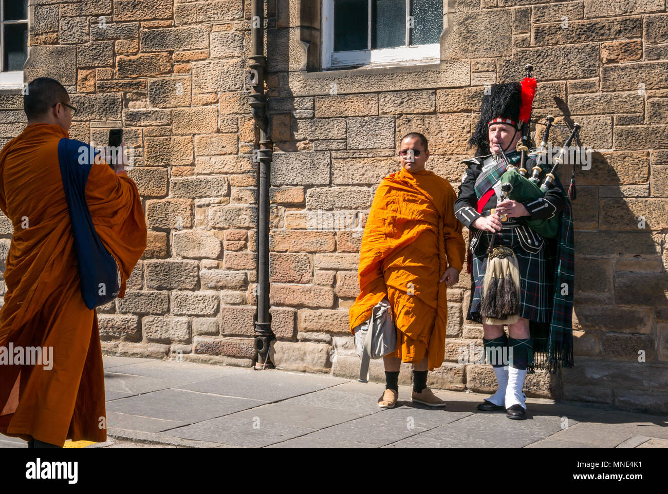 Royal Mile, Edinburgh, 16th May 2018. Tourists enjoying the sunshine on the Royal Mile, Edinburgh, Scotland, United Kingdom. Tourists throng the Royal Mile, including a group of Buddhist monks dressed in bright orange robes. A buddhist monk is taking a photo of a Buddhist monk standing next to a Scottish bagpipe player dressed in a kilt Stock Photo