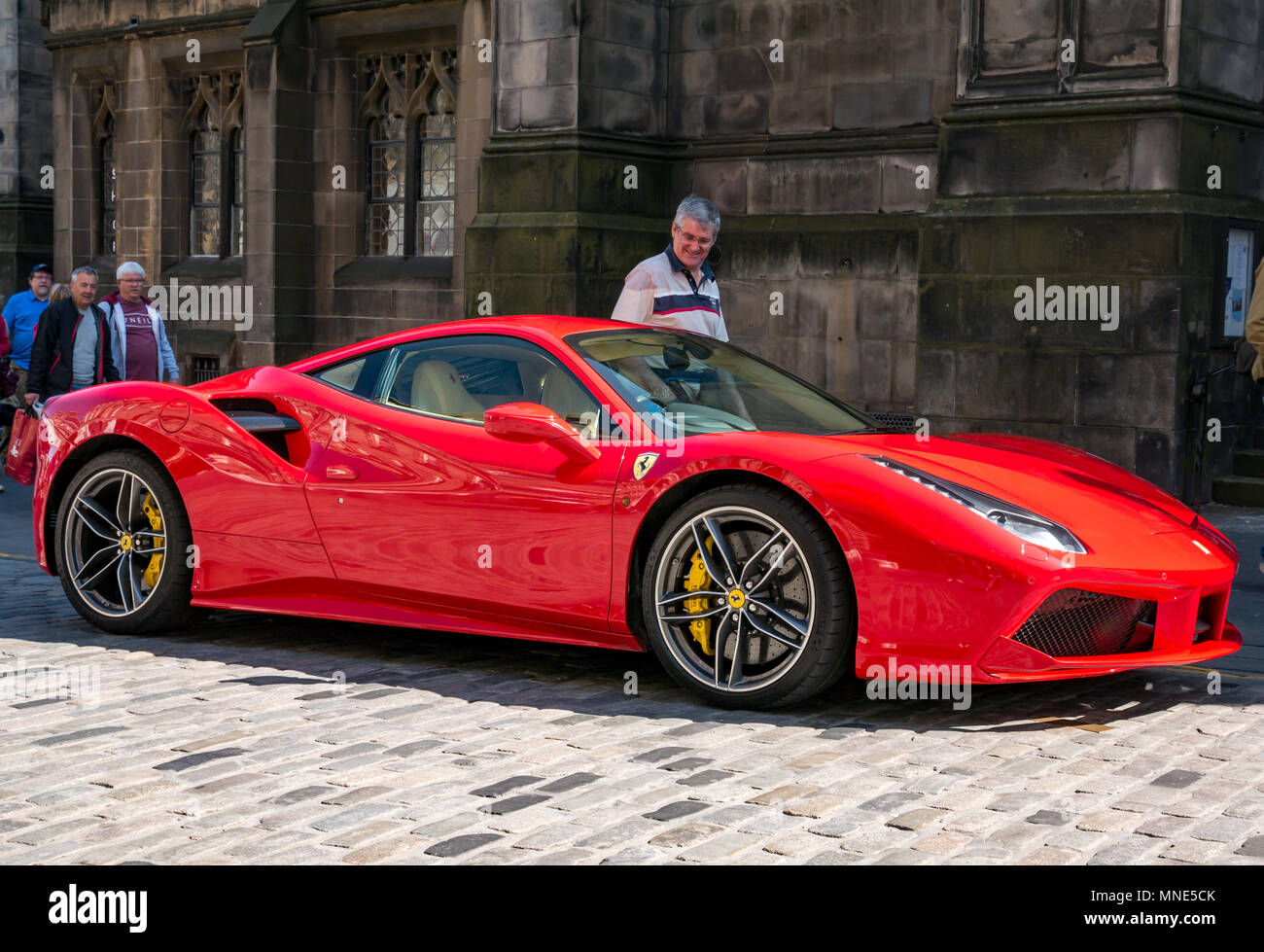 Royal Mile, Edinburgh, 16th May 2018. Tourists enjoying the sunshine on the Royal Mile, Edinburgh, Scotland, United Kingdom. A man walks by a bright red Ferrari 488 GTB coupe sports car parked on a double yellow line on the cobbled Royal Mile next to St Giles Cathedral, giving it an envious look Stock Photo