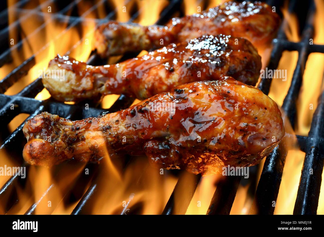 Three chicken legs in BBQ sauce cooking on a flaming grill Stock Photo