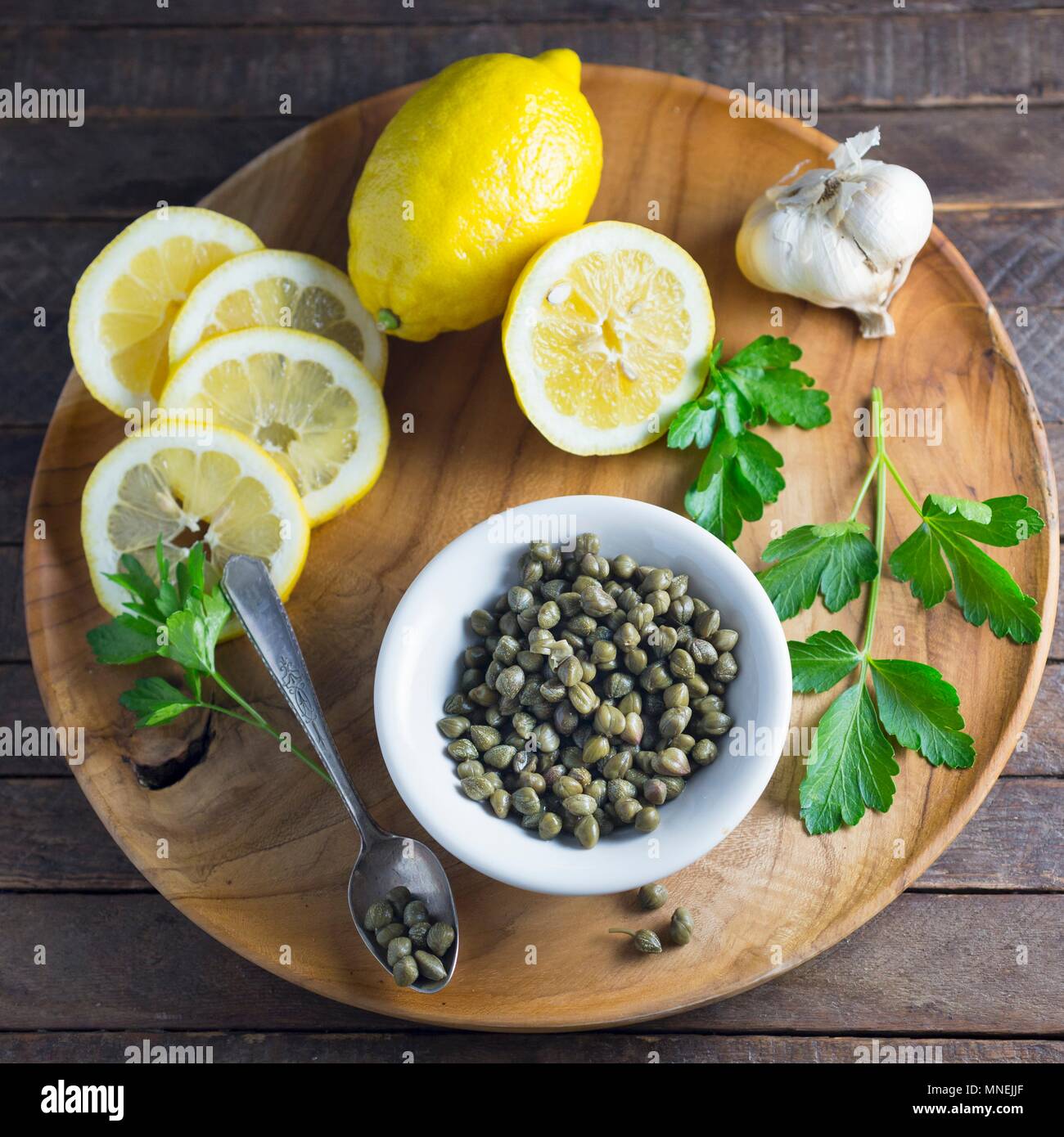 Lemons, capers, garlic and parsley on a wooden plate Stock Photo