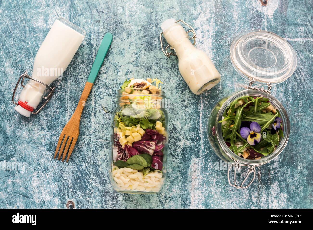 Quinoa and orzo pasta salads in glass jars, with dressing and a wooden fork Stock Photo