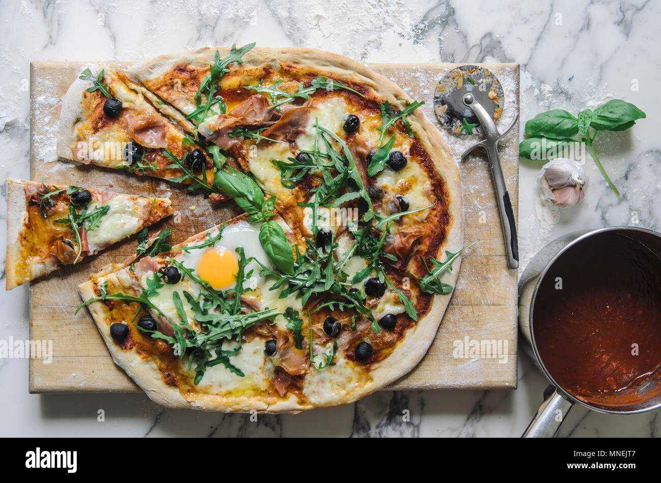 Pizza with tomato sauce, fried egg, rocket, olives and parmesan (top view) Stock Photo