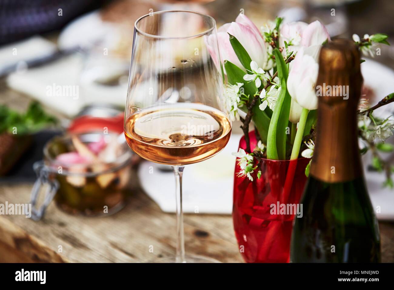 A glass of rosé champagne, a bunch of spring flowers and a bottle of champagne on a wooden table Stock Photo