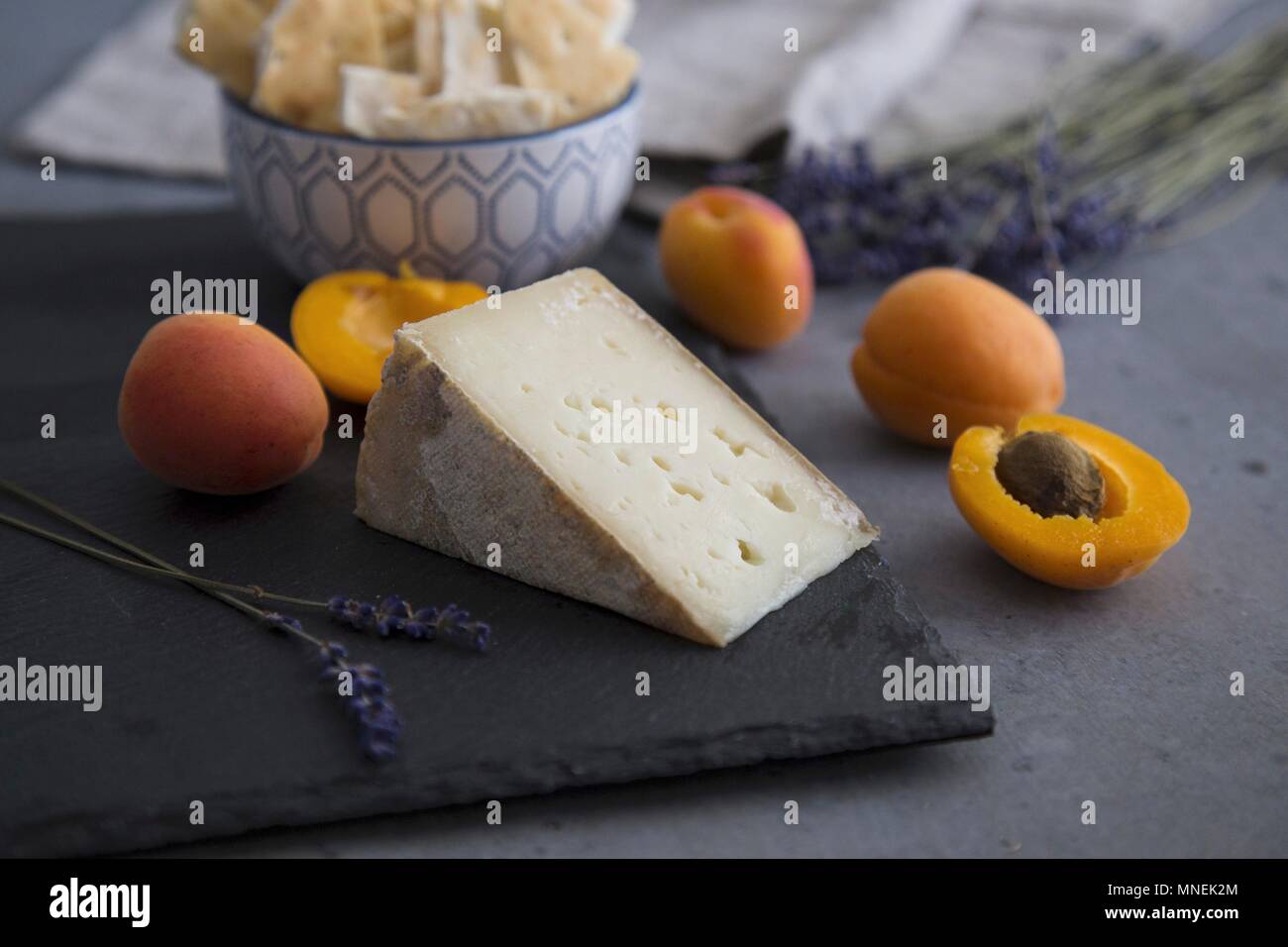 Apricots and goat's cheese on a slate platter with crackers and lavender flowers Stock Photo