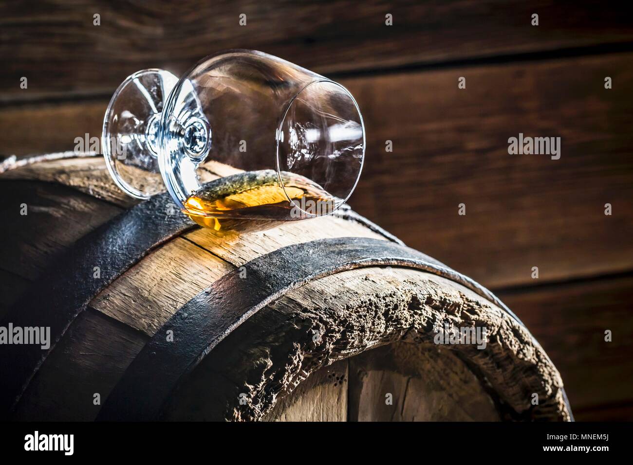 A overturned glass of cognac on an old wooden barrel Stock Photo