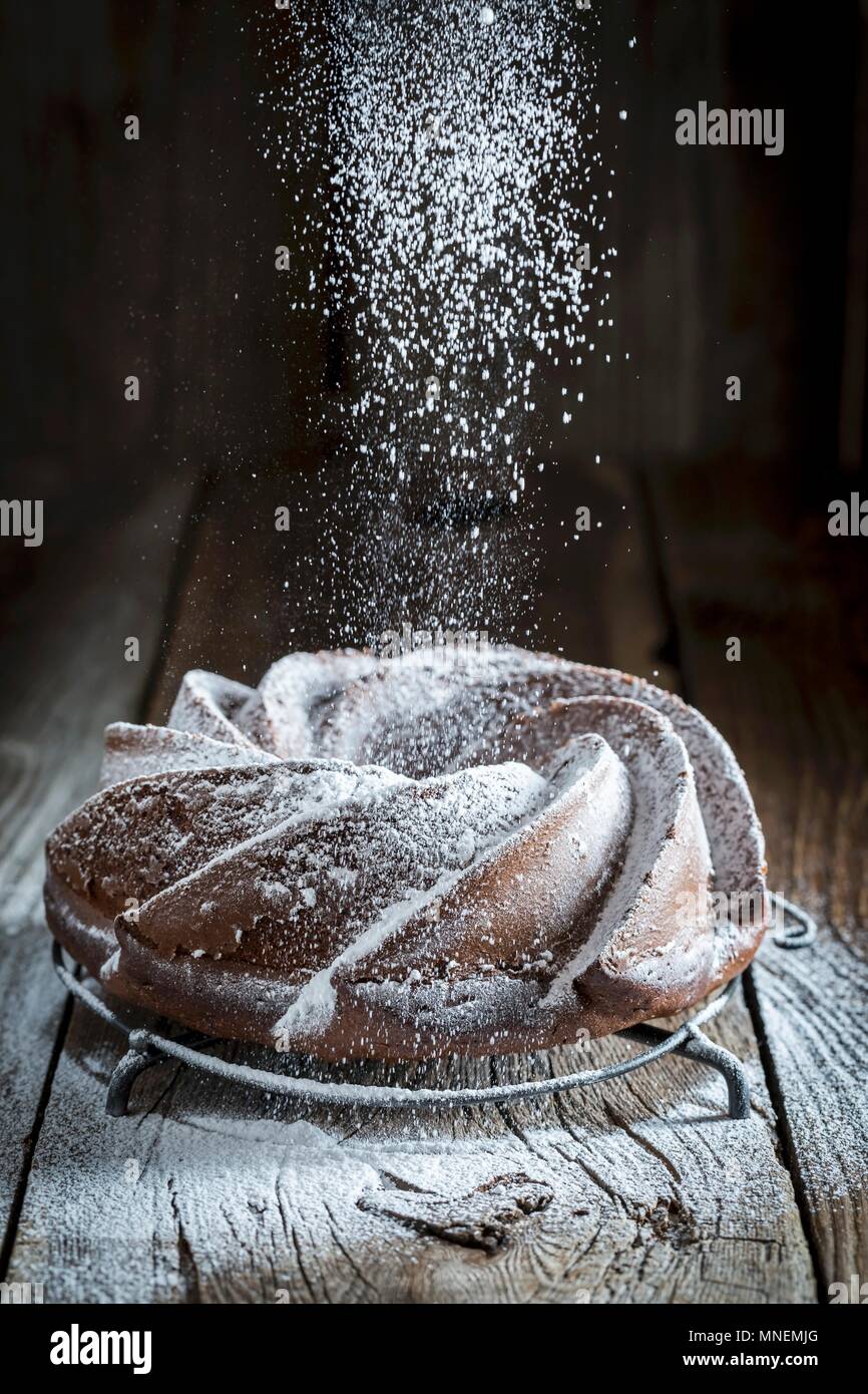 A Bundt cake on a wooden table being dusted with icing sugar Stock Photo