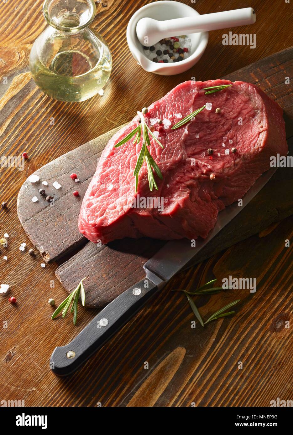 Raw beef fillet (450 g) on a wooden board with rosemary and colourful pepper Stock Photo