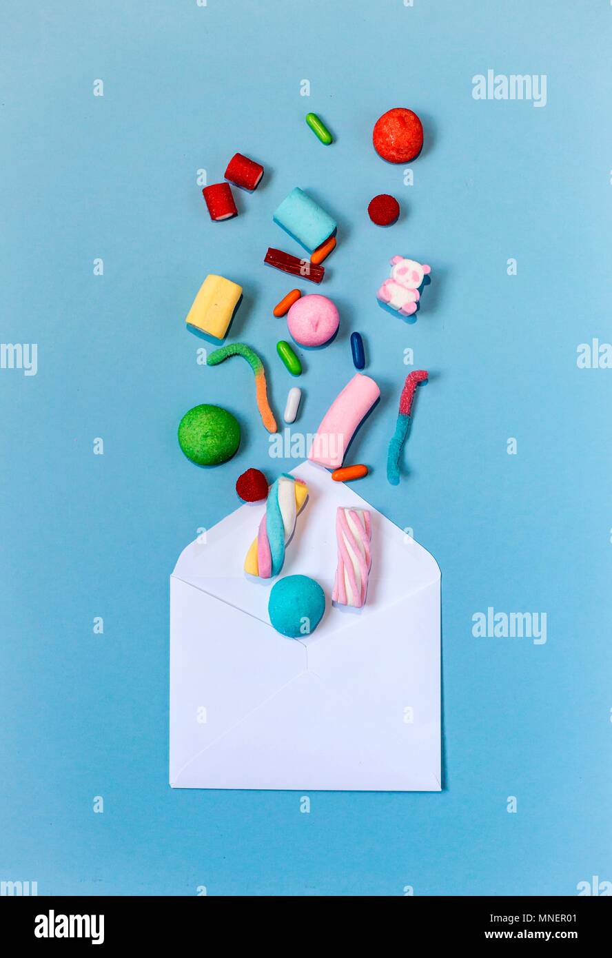 Colourful sweets coming out of an envelope on a light-blue background Stock Photo