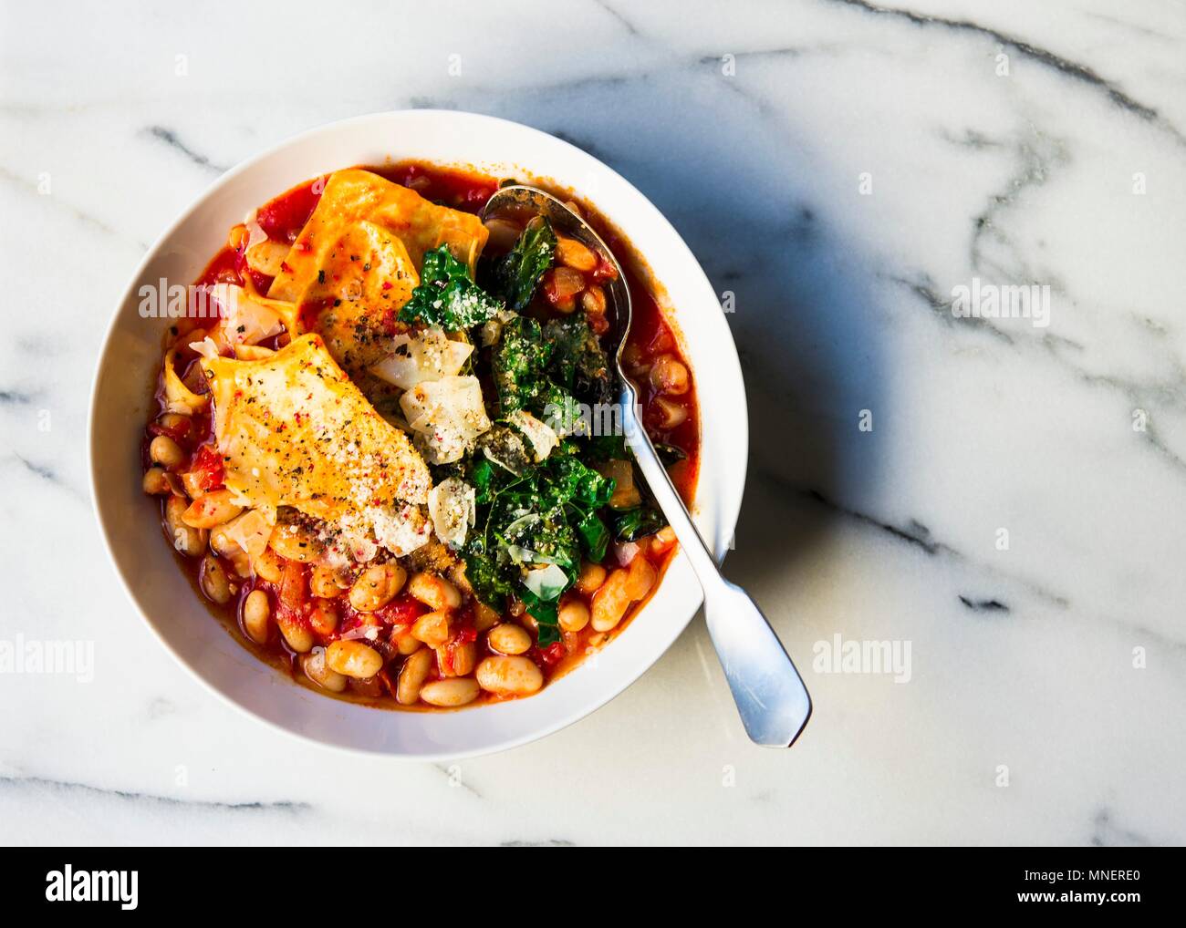 Cannelleni beans with pasta pieces in a tomato based soup topping with kale and cheese Stock Photo