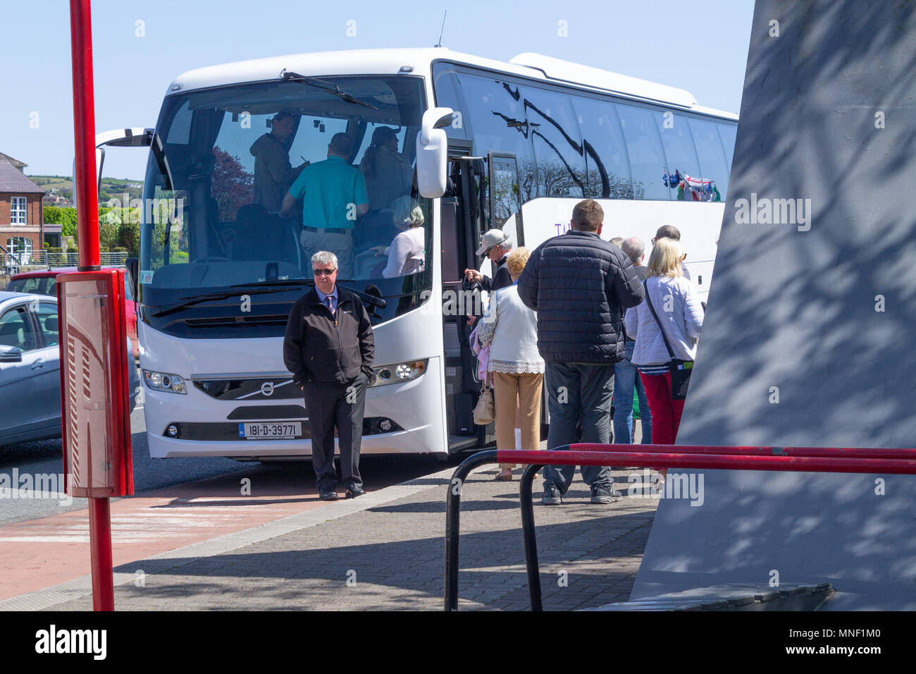 tourists standing in a queue waiting to board a coach on a day out in kinsale ireland , a popular holiday seaside town. Stock Photo