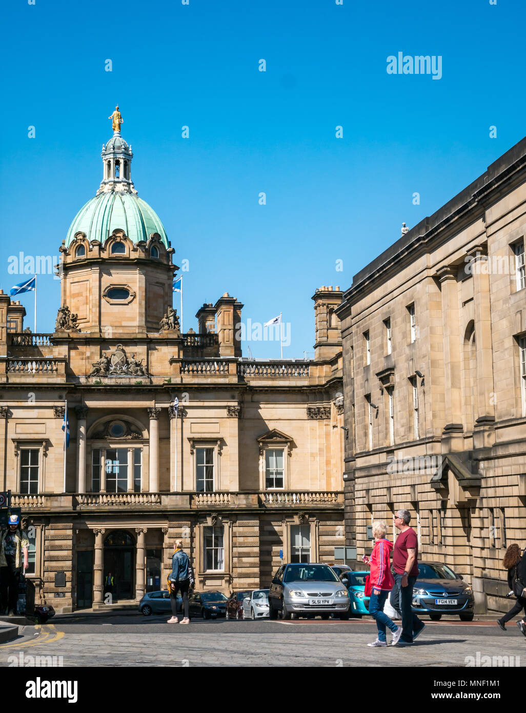 Tourists walking on Royal Mile crossing road past grand building of Bank of Scotland headquarters with copper dome and blue sky Stock Photo