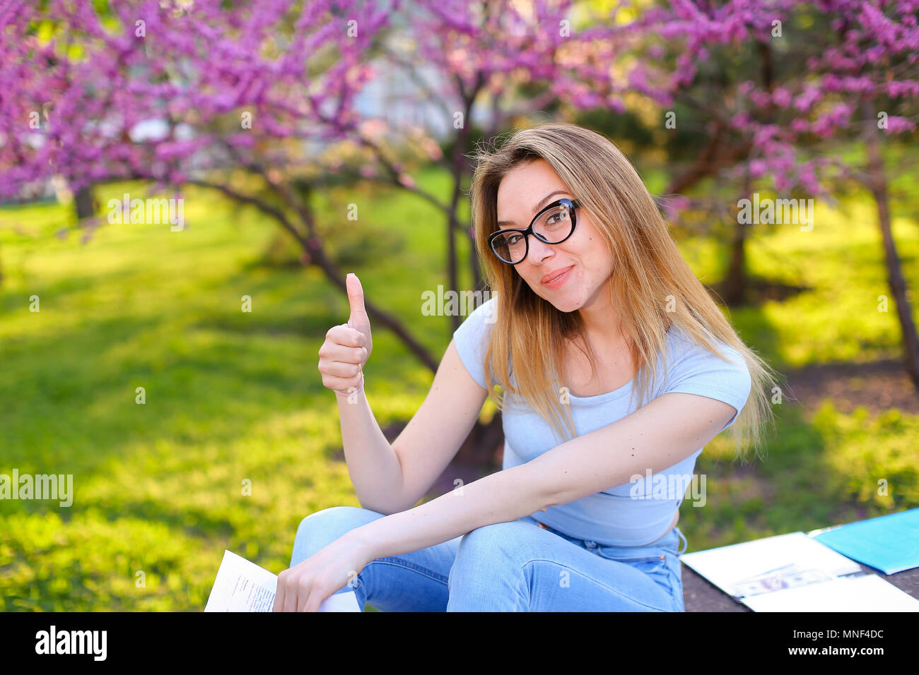 Female student studying in park and showing thumbs up Stock Photo - Alamy