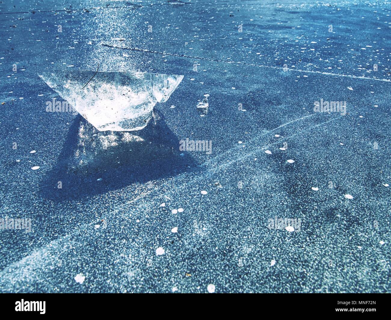 Ice shards on a frozen lake. The rays of the sun creat rainbow shadows in the cracks of the ice. Stock Photo