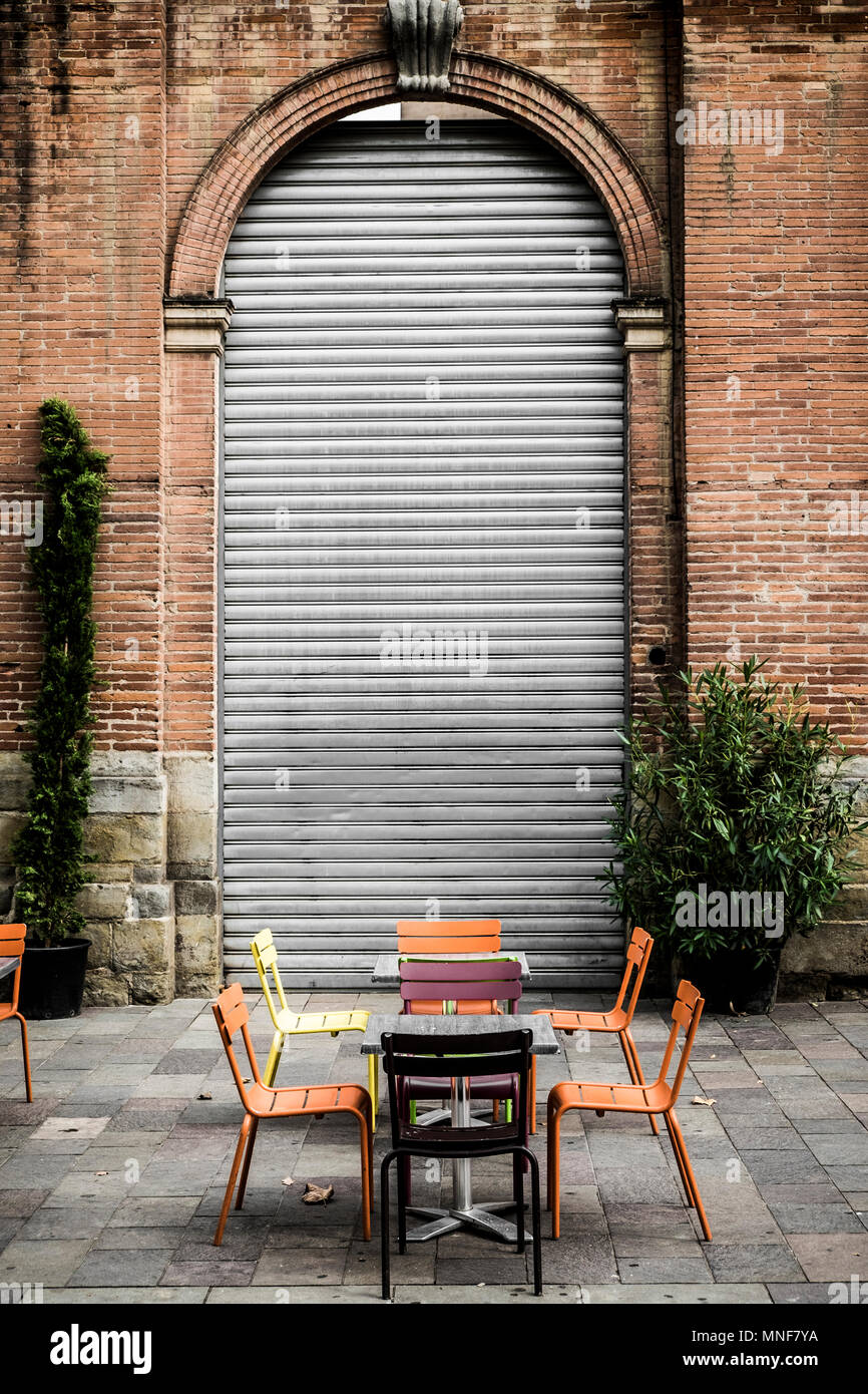 Table with coloured chairs in a street in front of closed door, Toulouse, France Stock Photo