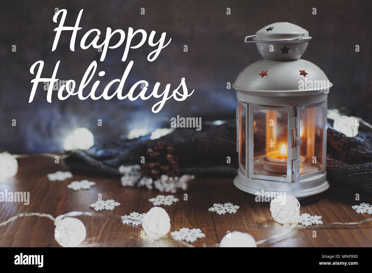 Cozy winter home. Lantern, candle, garland, snowflakes, pine cone, knitted gray sweater on a wooden table. The atmosphere of a New Year's fairy tale.  Stock Photo
