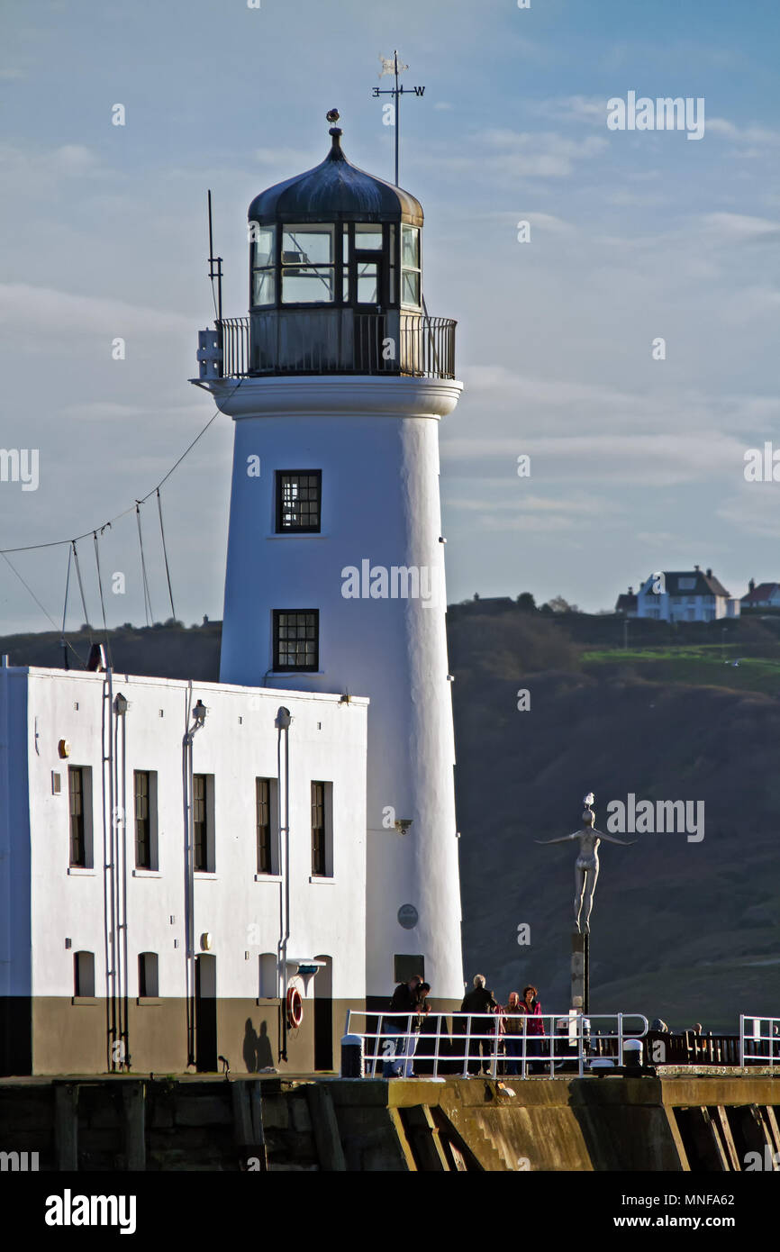 Scarborough’s Diving Belle statue stands dwarfed alongside the town’s lighthouse at the harbour entrance, against the backdrop of Holbeck’s cliffs. Stock Photo