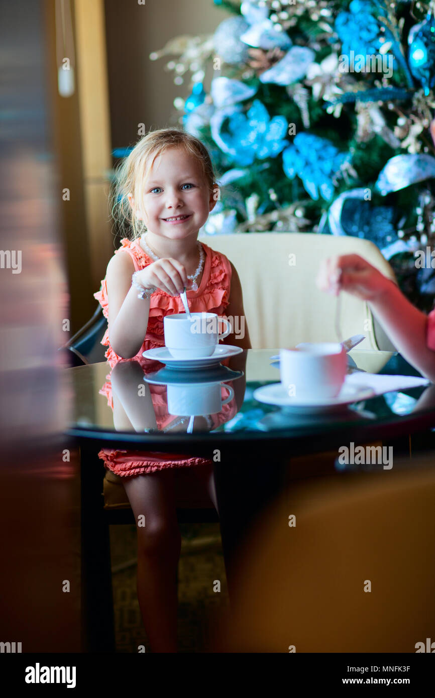 Little girl drinking tea from a white cup in a room decorated for Christmas Stock Photo