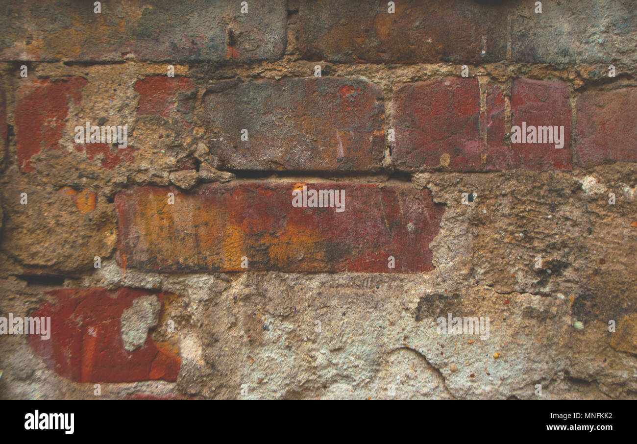 Old dark brick wall background with damaged plaster. Stock Photo