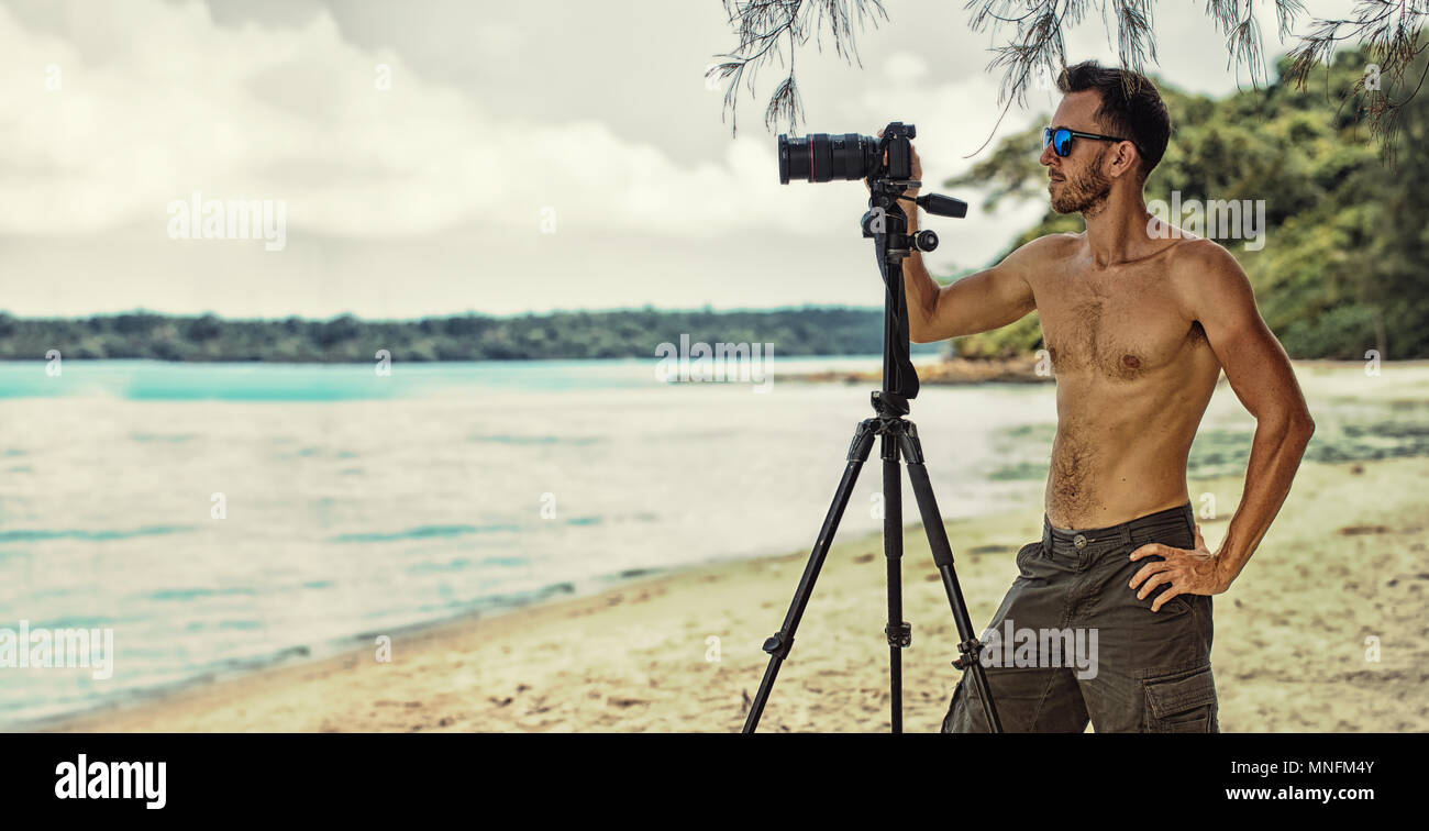man freelancer working outdoor, holding in hands digital camera and doing photo and video shoot on the background of scenery nature Stock Photo