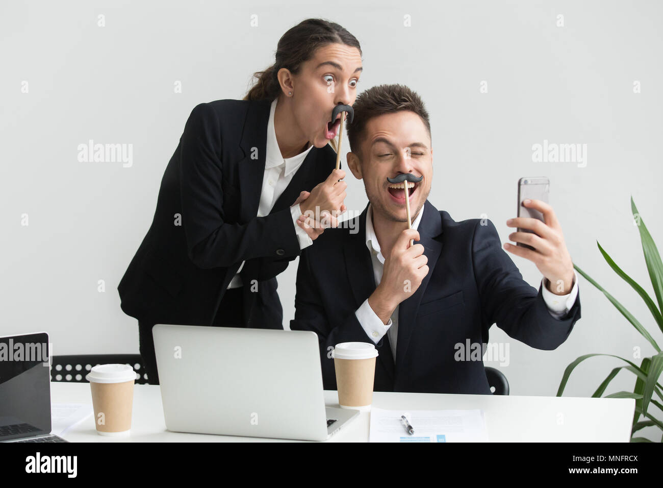 Colleagues making self-portrait with mustache accessory Stock Photo
