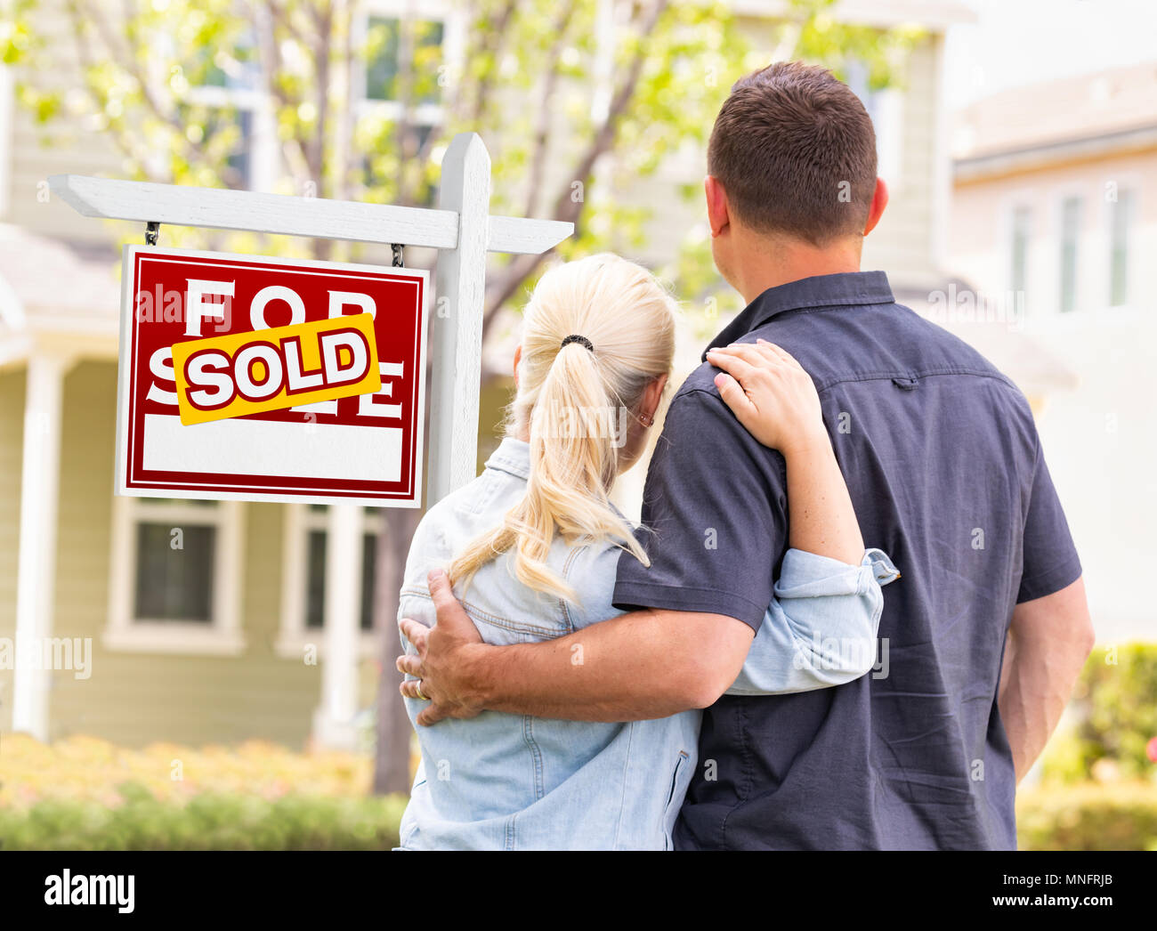 Caucasian Couple Facing Front of Sold Real Estate Sign and House. Stock Photo