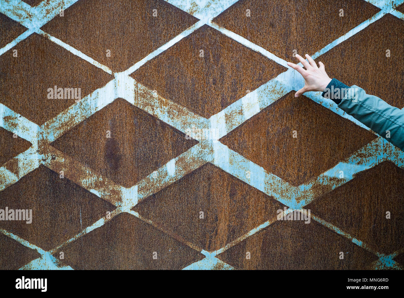 background of rusted vintage metal with a diamond pattern and vintage blue paint and a slender open female hand Stock Photo