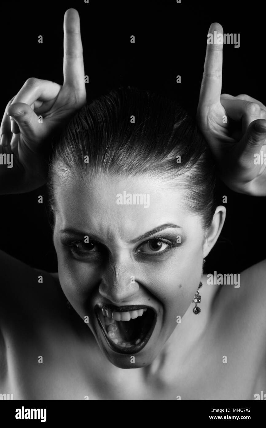 fun luxury woman show horns on black background, looking at camera, monochrome Stock Photo