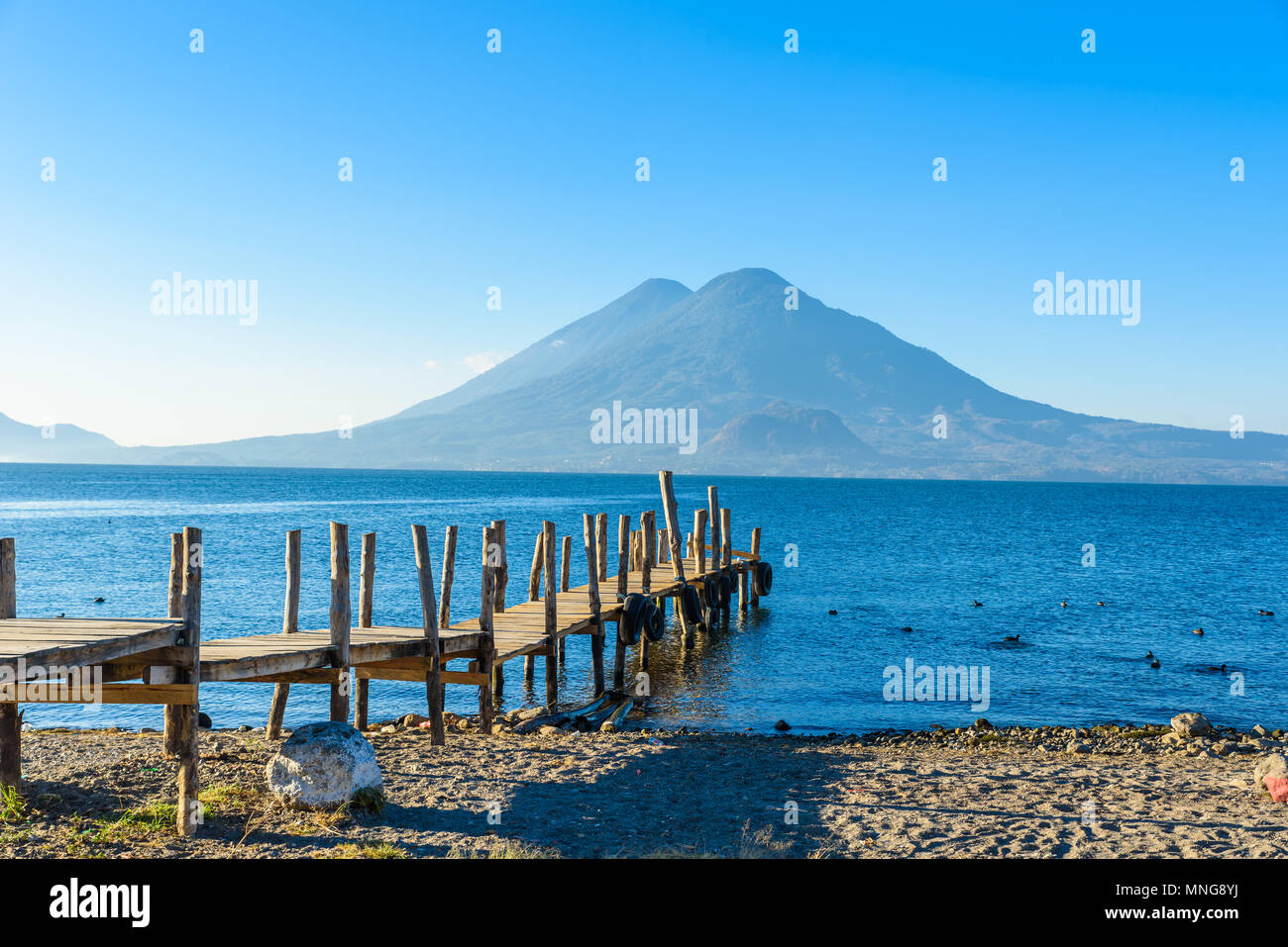 Wooden pier at Lake Atitlan on the beach in Panajachel, Guatemala.  With beautiful landscape scenery of volcanoes Toliman, Atitlan and San Pedro in th Stock Photo
