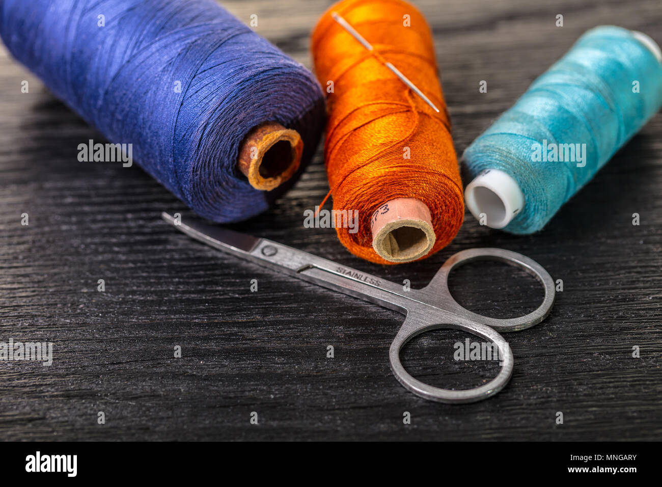 colored threads and scissors on a black wooden background Stock Photo