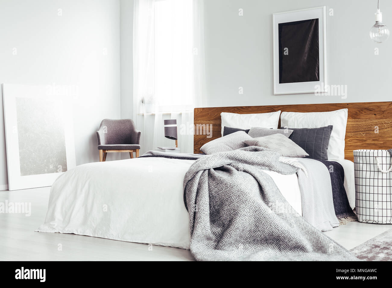Grey blanket on bed with wooden bedhead in simple bedroom interior with
