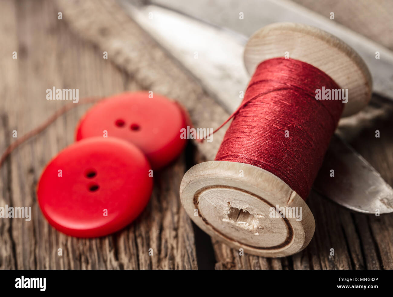 red thread with buttons and scissors, wooden background Stock Photo