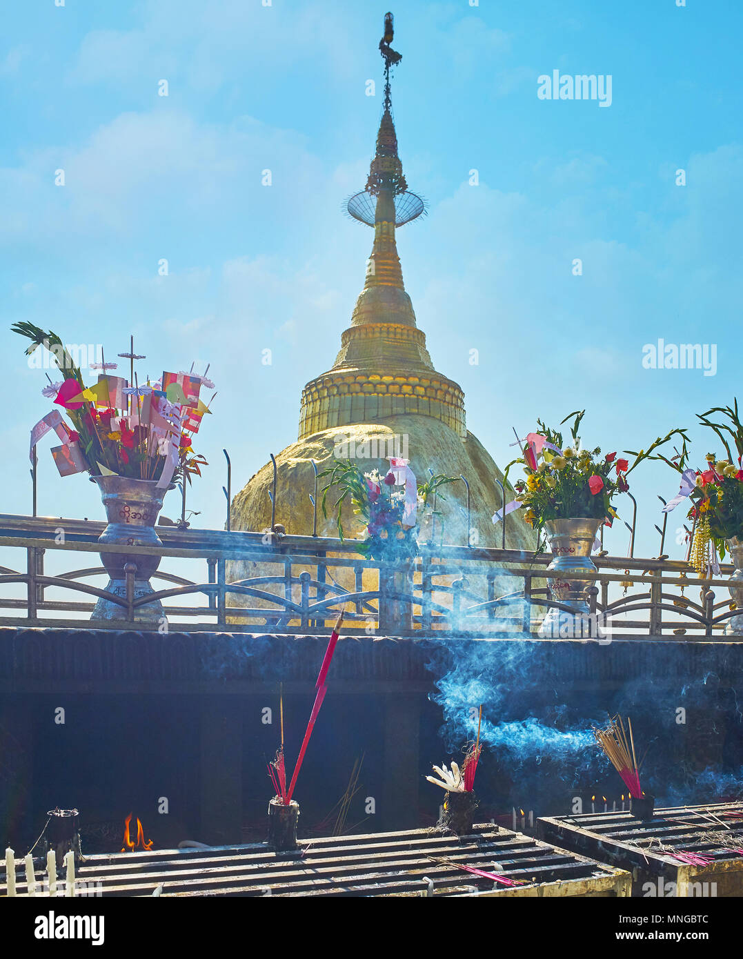 The outdoor altar with fuming incense sticks and burning candles in front of Kyite Htee Yoe Pagoda, built on the top of giant granite boulder on summi Stock Photo