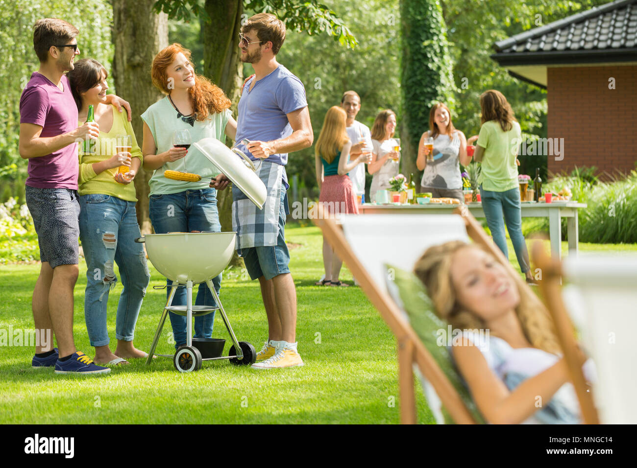 Young man grilling food while talking with friends Stock Photo