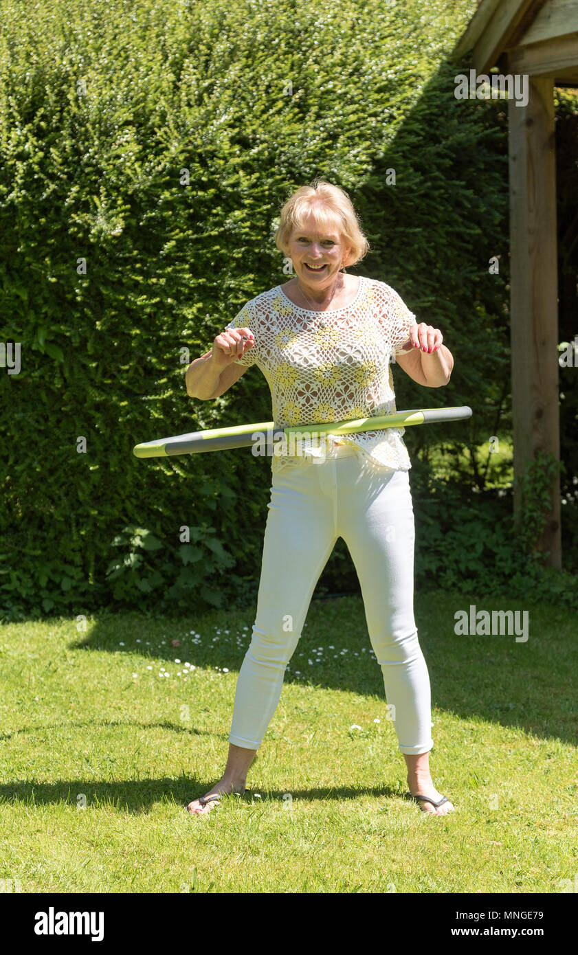 Woman using a hula hoop to exercise in a garden setting Stock Photo