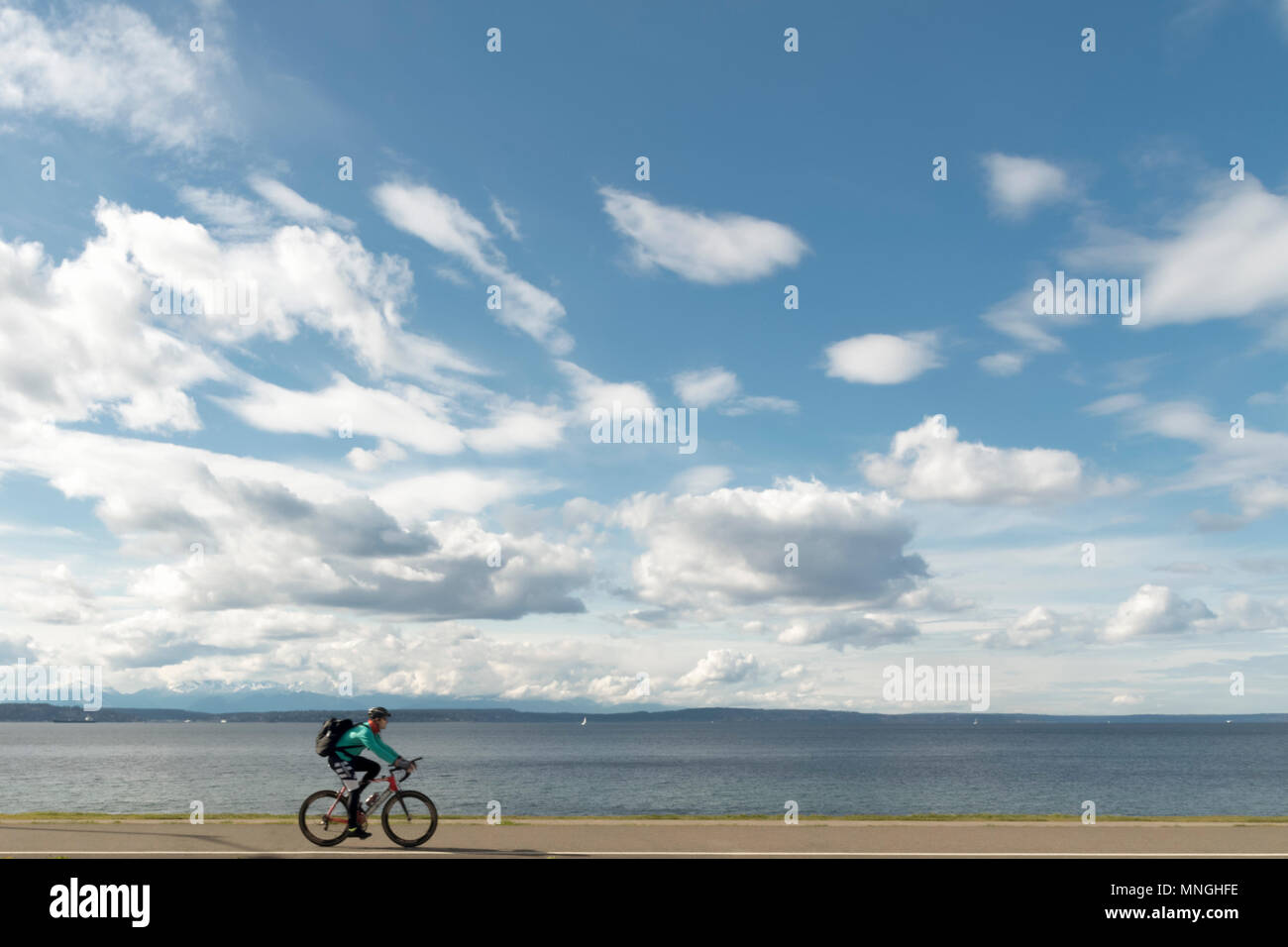 Man commuting on bicycle on a sunny afternoon next to Puget Sound near Seattle Washington. Stock Photo