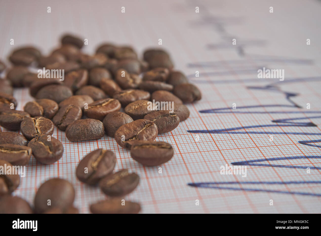 Loose roasted coffee beans on an ECG tracing showing an increased heart beat conceptual of coffee as a stimulant and its health implications Stock Photo