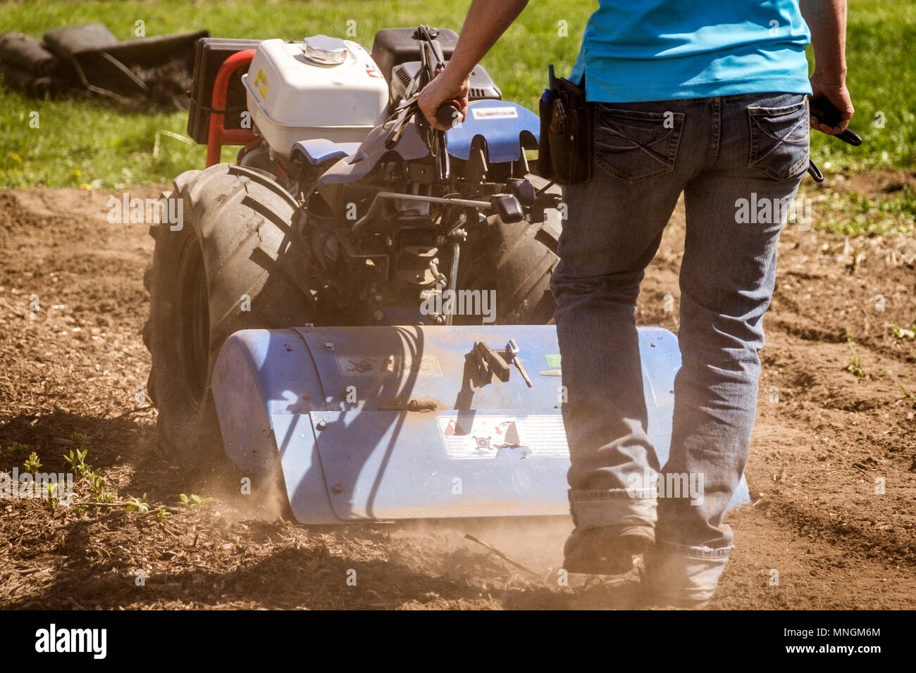 Woman worker driving rototiller tractor unit preparing soil on outdoor garden Stock Photo