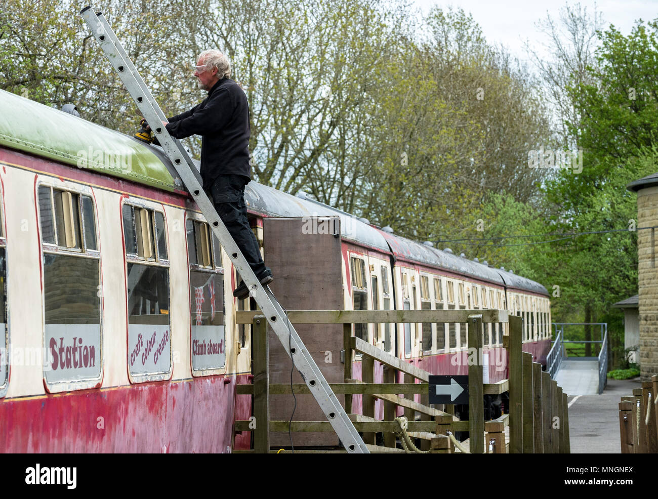 Man standing on a ladder sanding down the metal roof of a rail carrage. Stock Photo